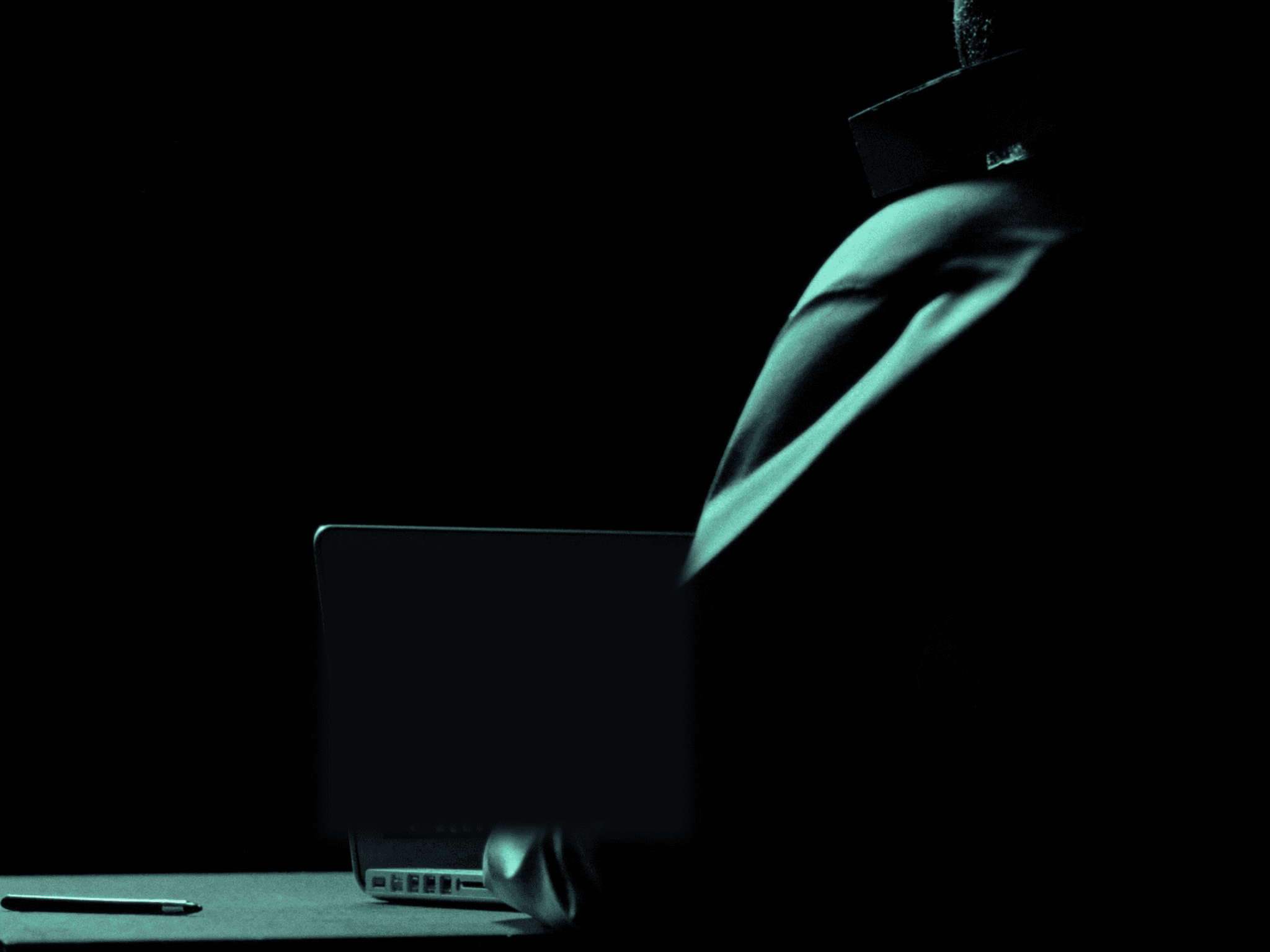 Persona trabajando de espaldas frente a una laptop, iluminación turquesa